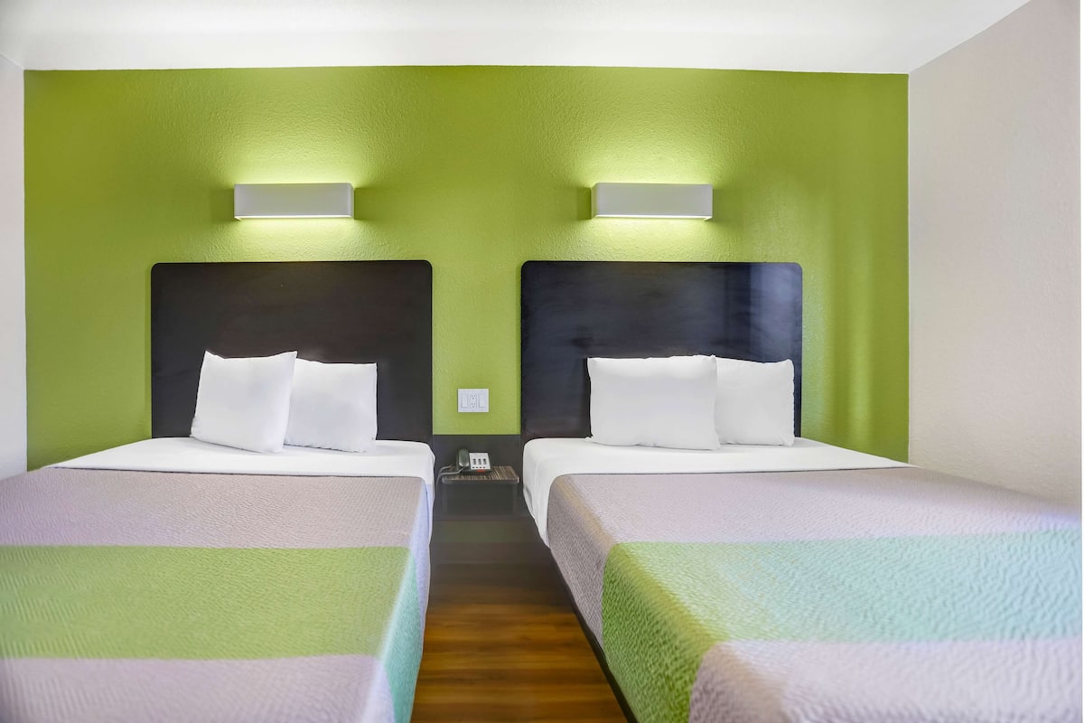 A hotel room with two beds, green walls, and a wooden floor.