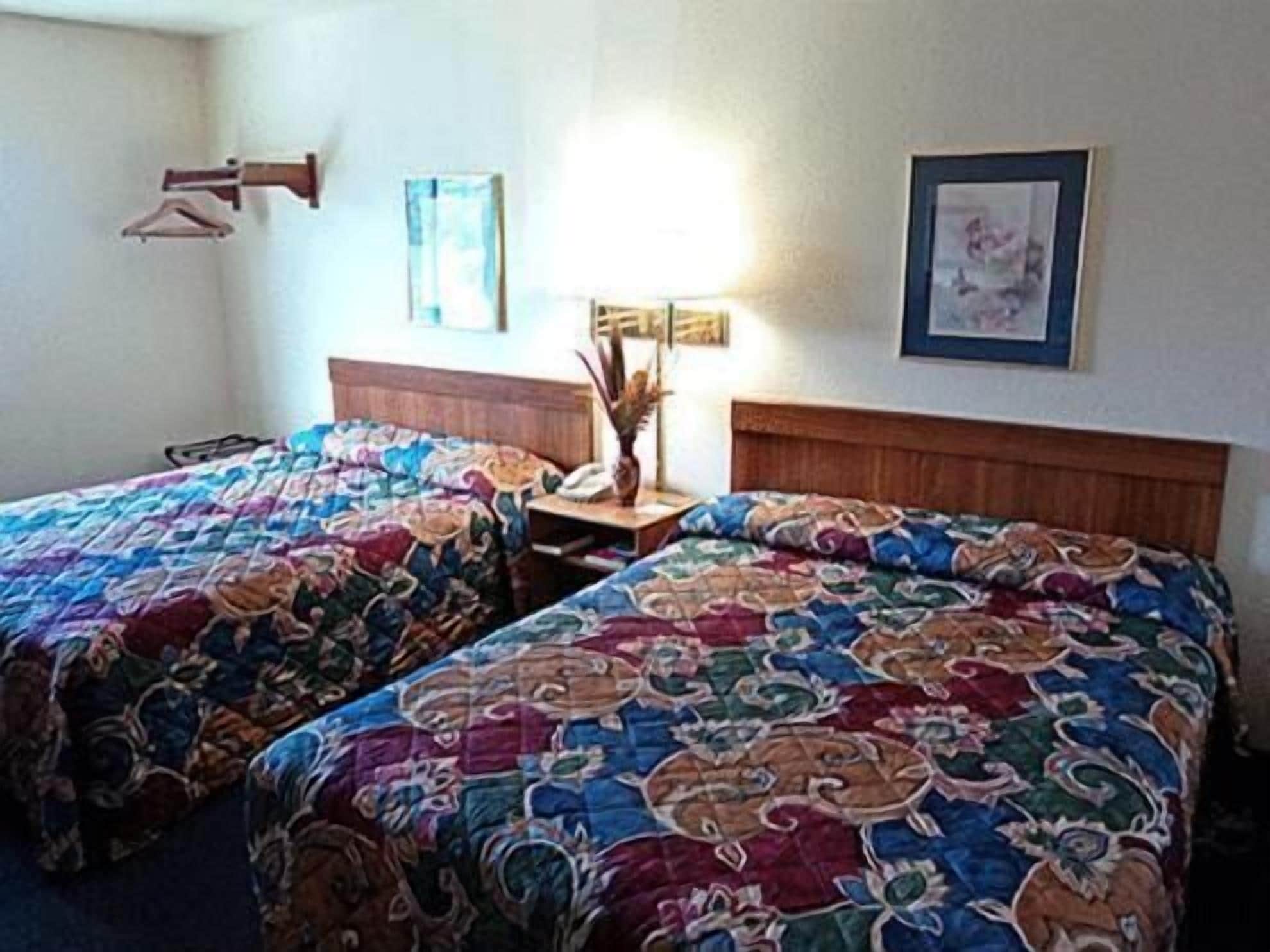 A hotel room with two single beds, a nightstand, a lamp, and a framed picture on the wall.