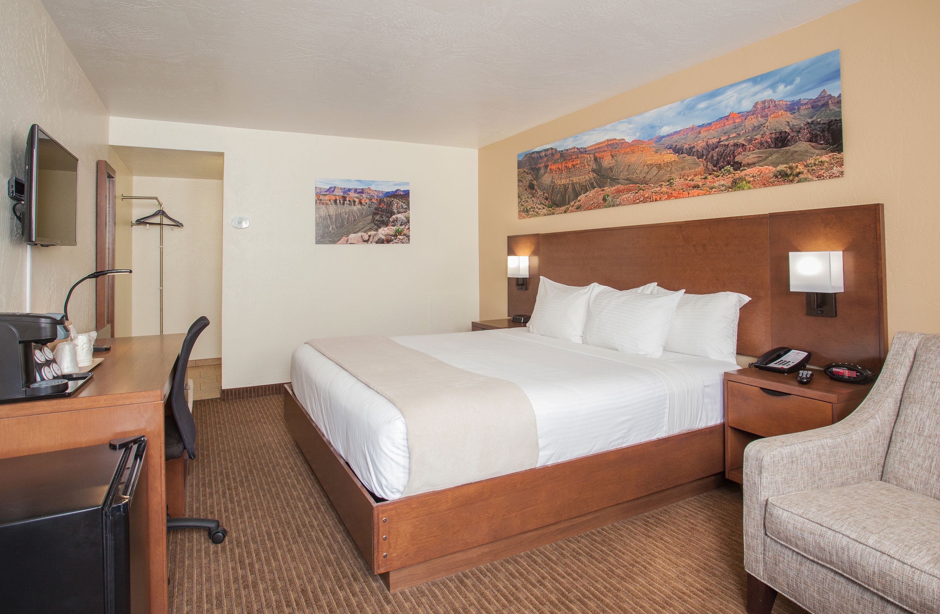 Hotelkamer met een groot bed, een bureau met koffiezetapparaat, een stoel en een schilderij van een canyonlandschap aan de muur.