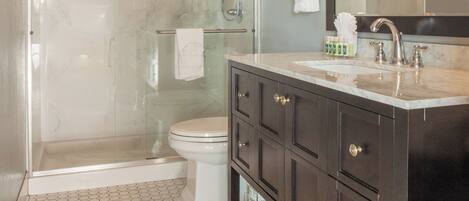 A modern bathroom with a glass-enclosed shower, a white toilet, and a dark wooden vanity with a large mirror.