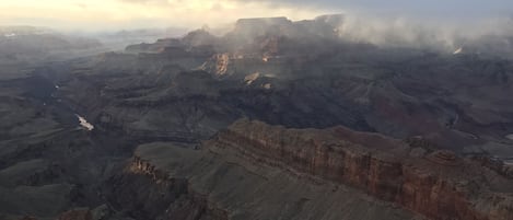 Un vaste paysage de canyon, avec des formations rocheuses en strates et une rivière qui traverse le terrain.