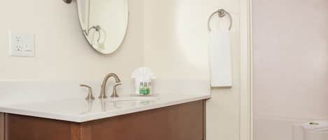 A bathroom with a wooden vanity, a large mirror, a towel rack, and a shower area.
