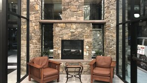 A lobby with a stone fireplace, two leather chairs, and a small table.