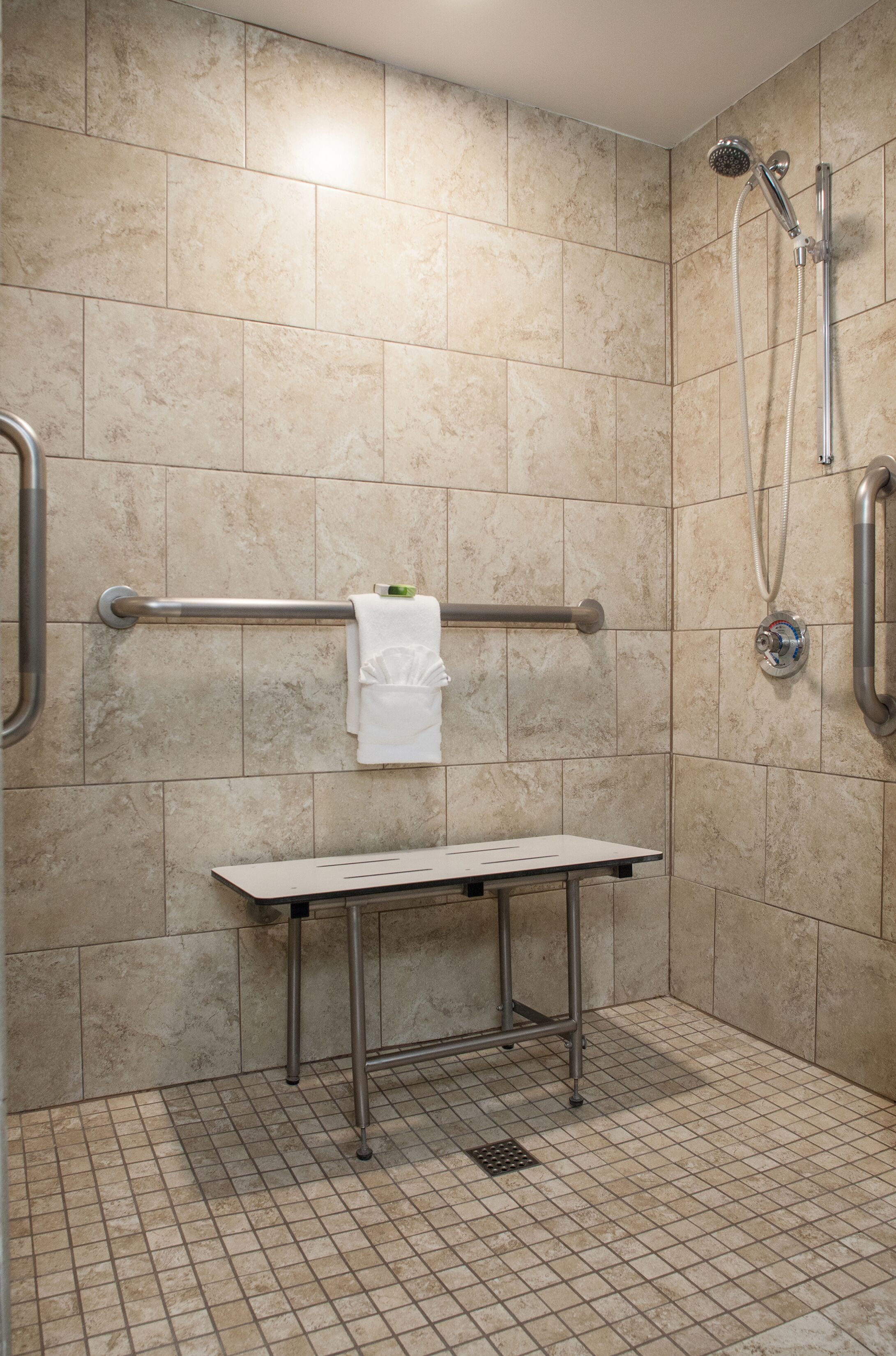 A shower area with beige tiles, a grab bar, a towel rack, and a small table.