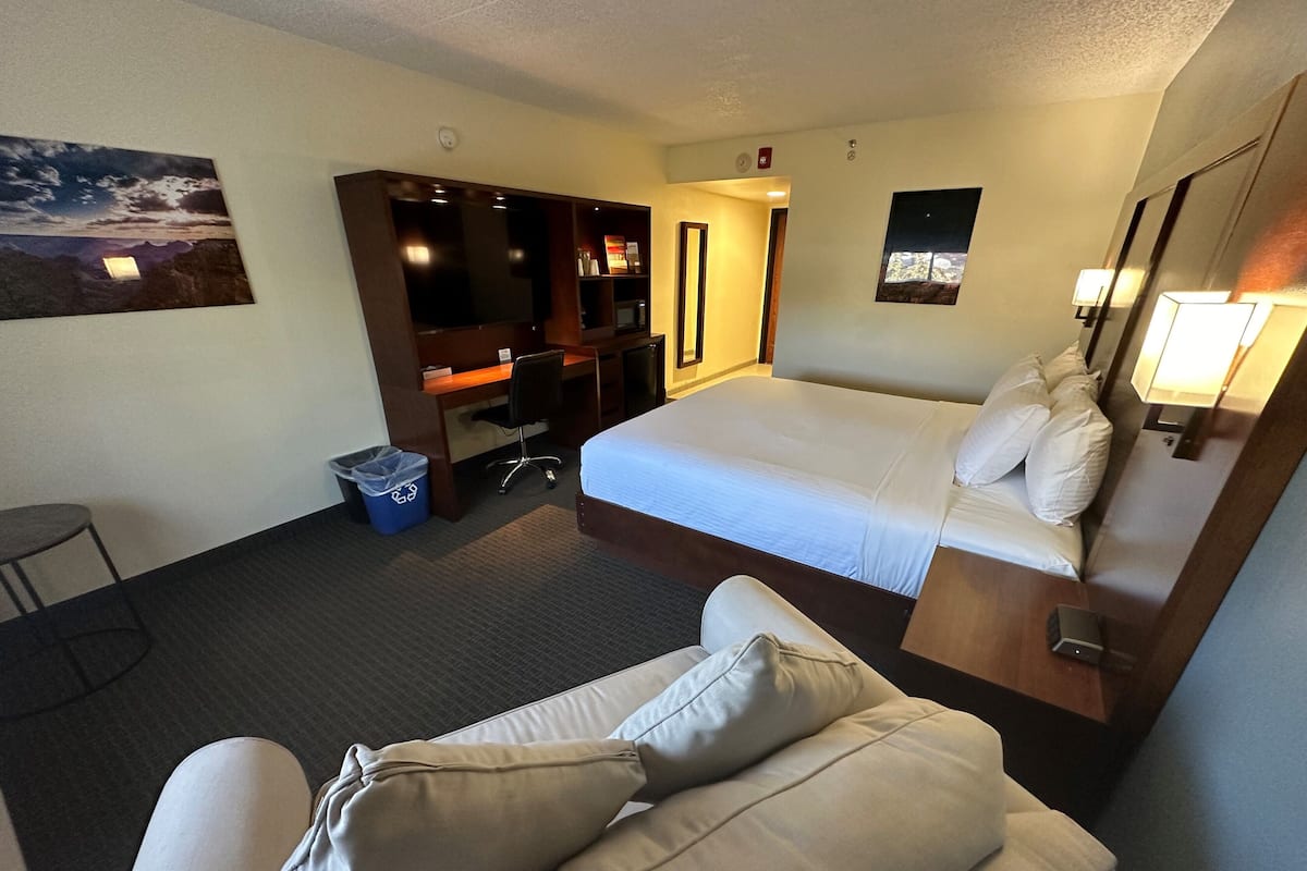 Habitación de hotel con cama, escritorio, silla, una mesita y un cesto de basura.