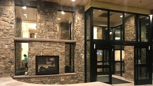 A stone-walled lobby with a fireplace, glass doors, and a tiled floor.