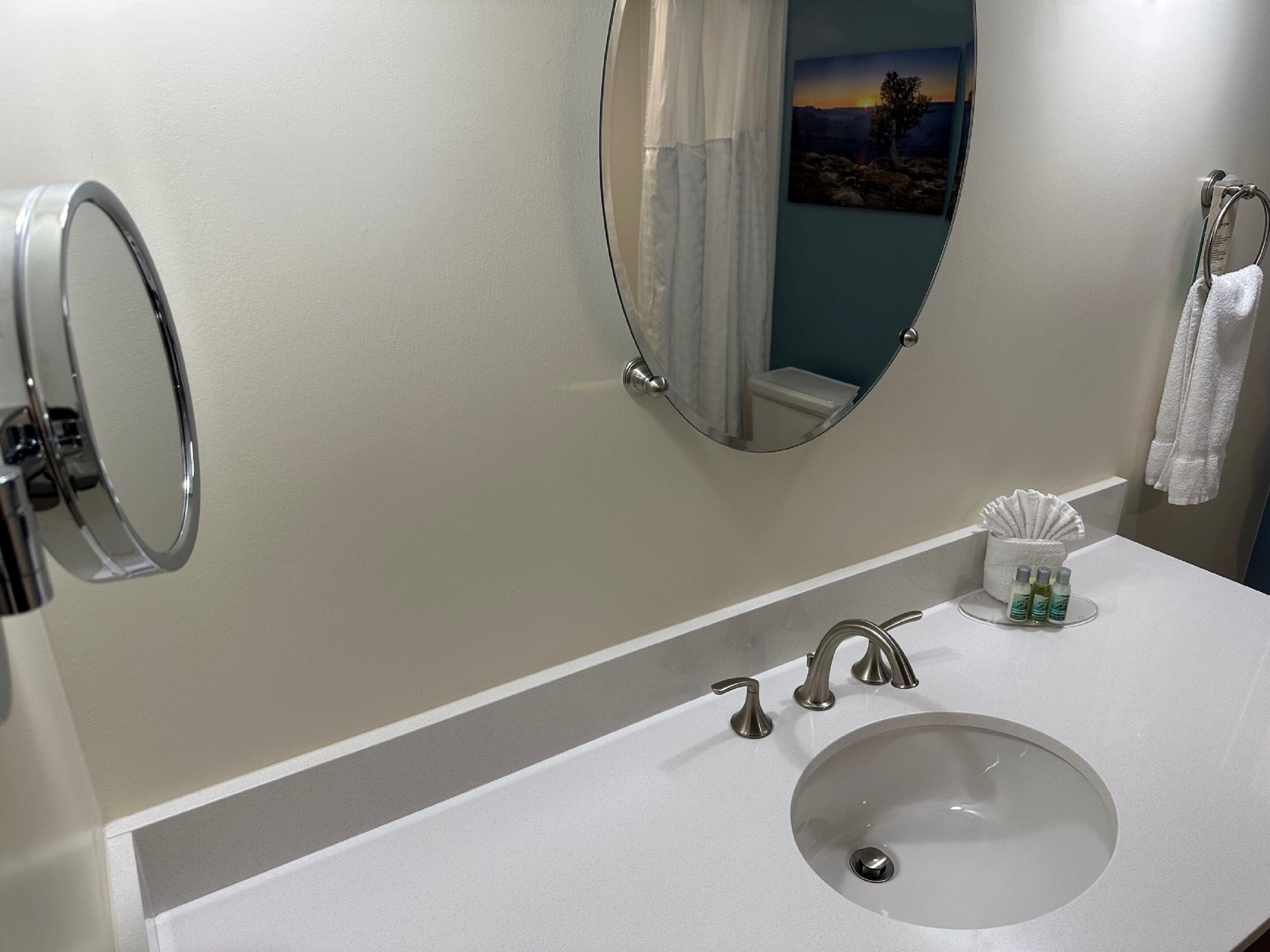 Un baño con lavamanos blanco, dos llaves, un espejo y un perchero para toallas.