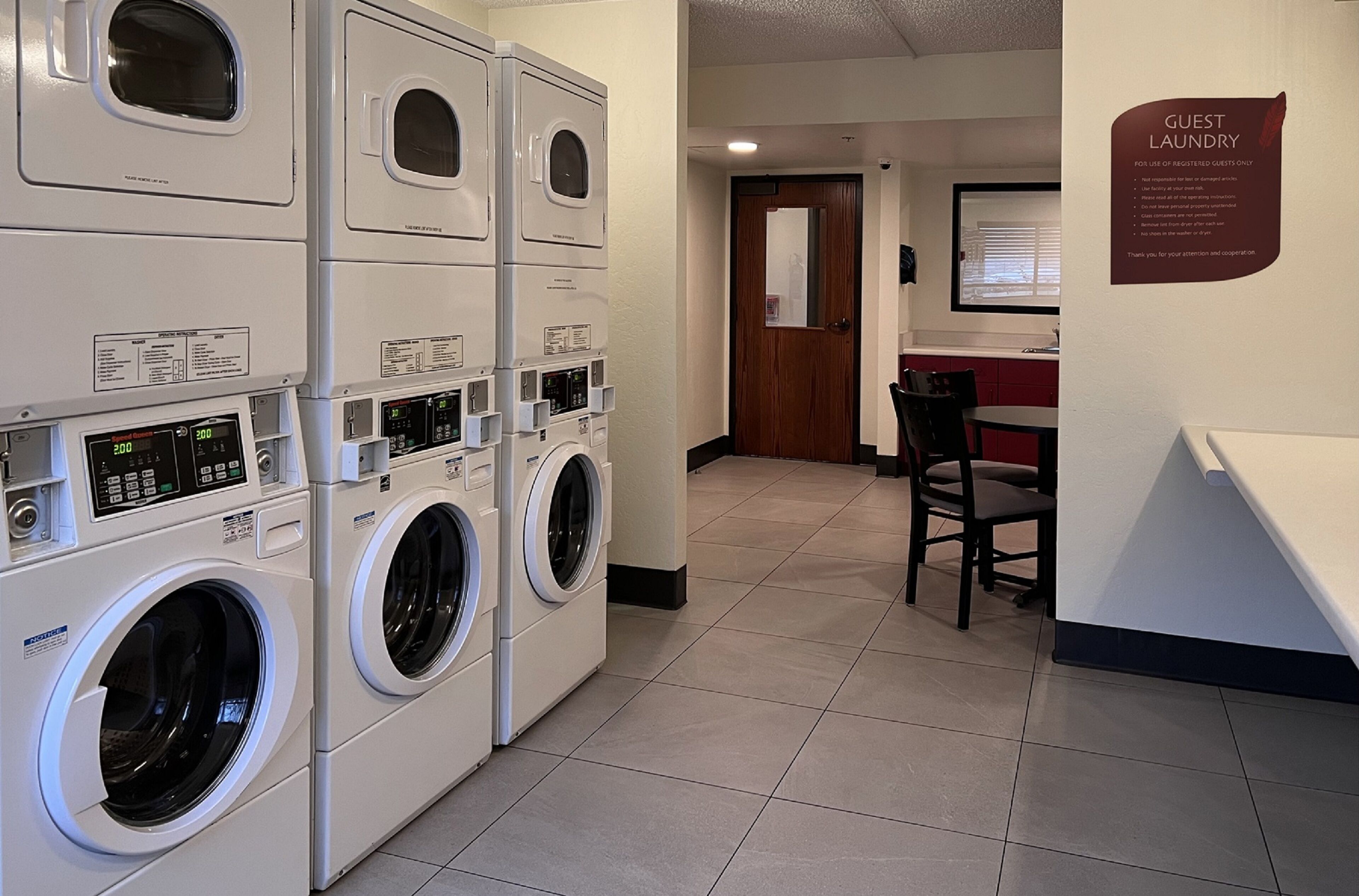 A hotel laundry area with multiple washing machines, a guest table, and a sign indicating guest laundry use.
