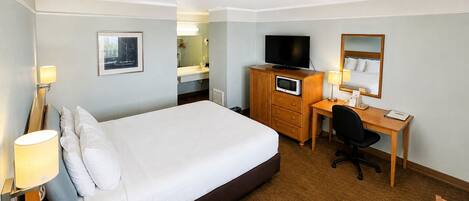 Ein Hotelzimmer mit Bett, Schreibtisch, Stuhl, Fernseher und einem durchgegangenen Tür sichtbaren Badezimmer.
