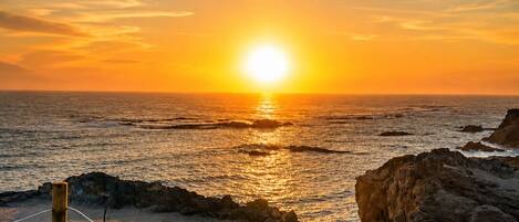 Un atardecer sobre un paisaje costero con un litoral rocoso y un primer plano cubierto de hierba.