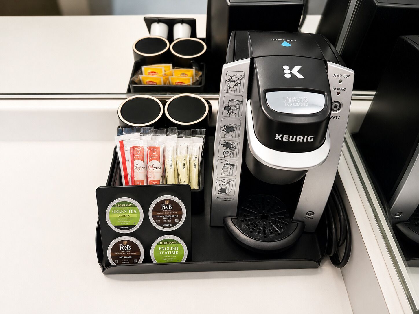 Een Keurig koffiezetapparaat met een waterreservoir, een houder voor koffiekapsules en een bakje met koffiekapsules.