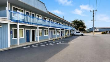 A motel with a row of rooms, a parking lot, and a clear sky.