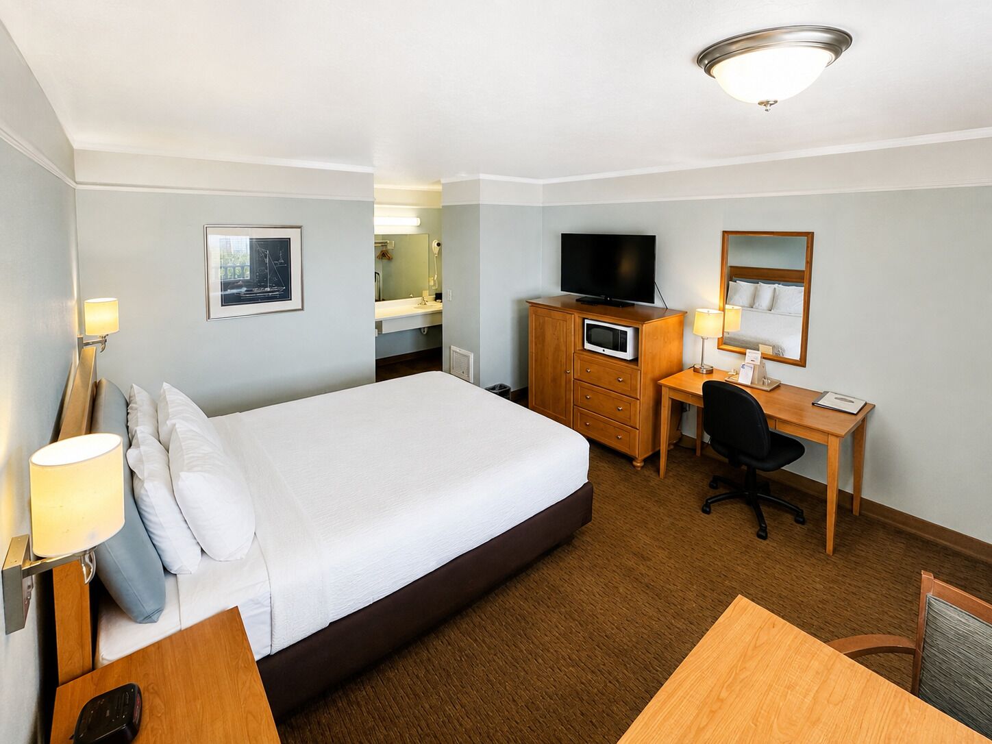 Habitación de hotel con una cama grande, un escritorio, una silla, un televisor y un espejo.