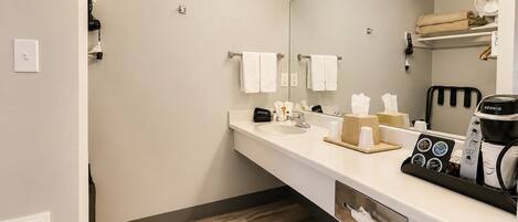 A modern bathroom with a white sink, mirror, and a coffee machine.