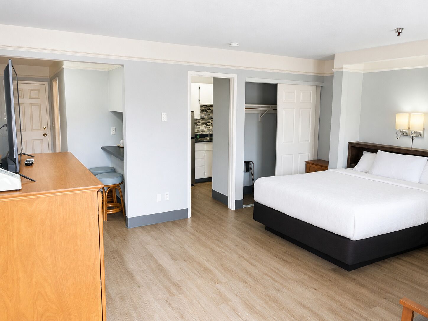 A hotel room with a bed, a desk with a computer, a chair, a wardrobe, and a bathroom visible through an open door.