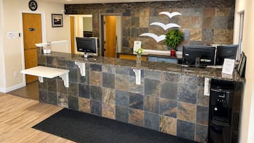 Zona de recepción con mostrador de piedra, dos monitores, una planta y un refrigerador.