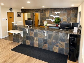 A reception area with a stone counter, two monitors, a plant, and a refrigerator. - Seabird Lodge (Fort Bragg)