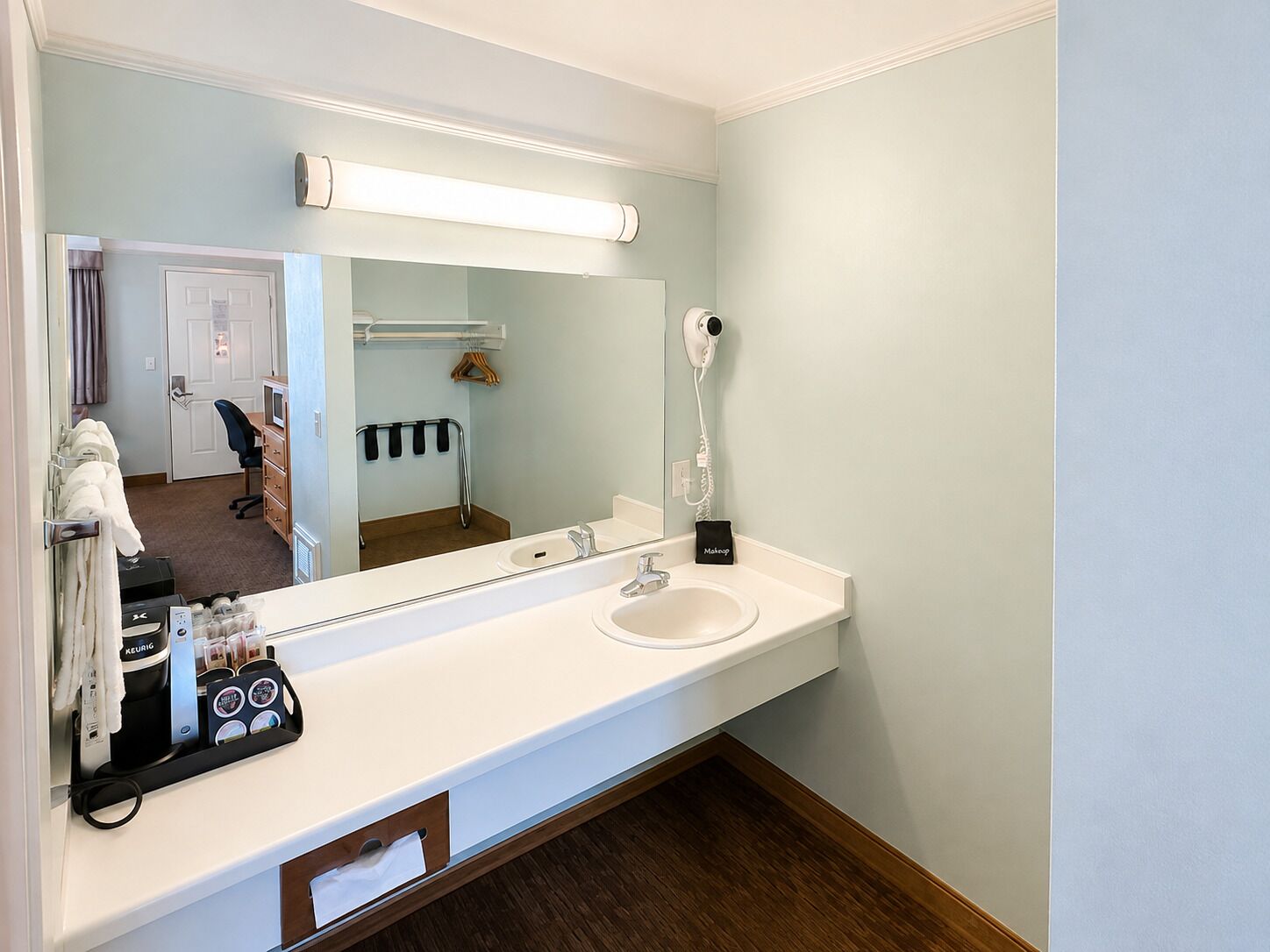 Een badkamer met een witte wastafel, een spiegel, een haardroger en een handdoekhouder.