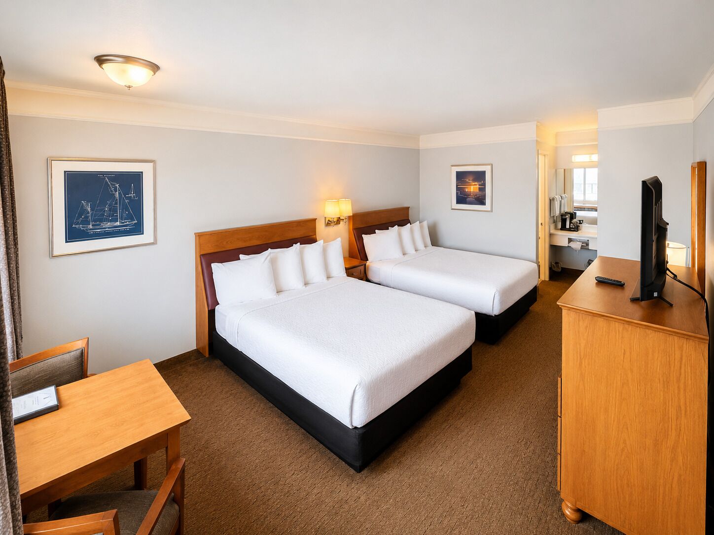 A hotel room with two beds, a desk, a TV, and a bathroom visible through an open door.