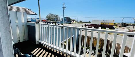 A balcony with a white railing overlooking a parking area and buildings.