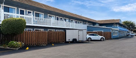 A row of two-story motel buildings with white railings and a fenced parking area.