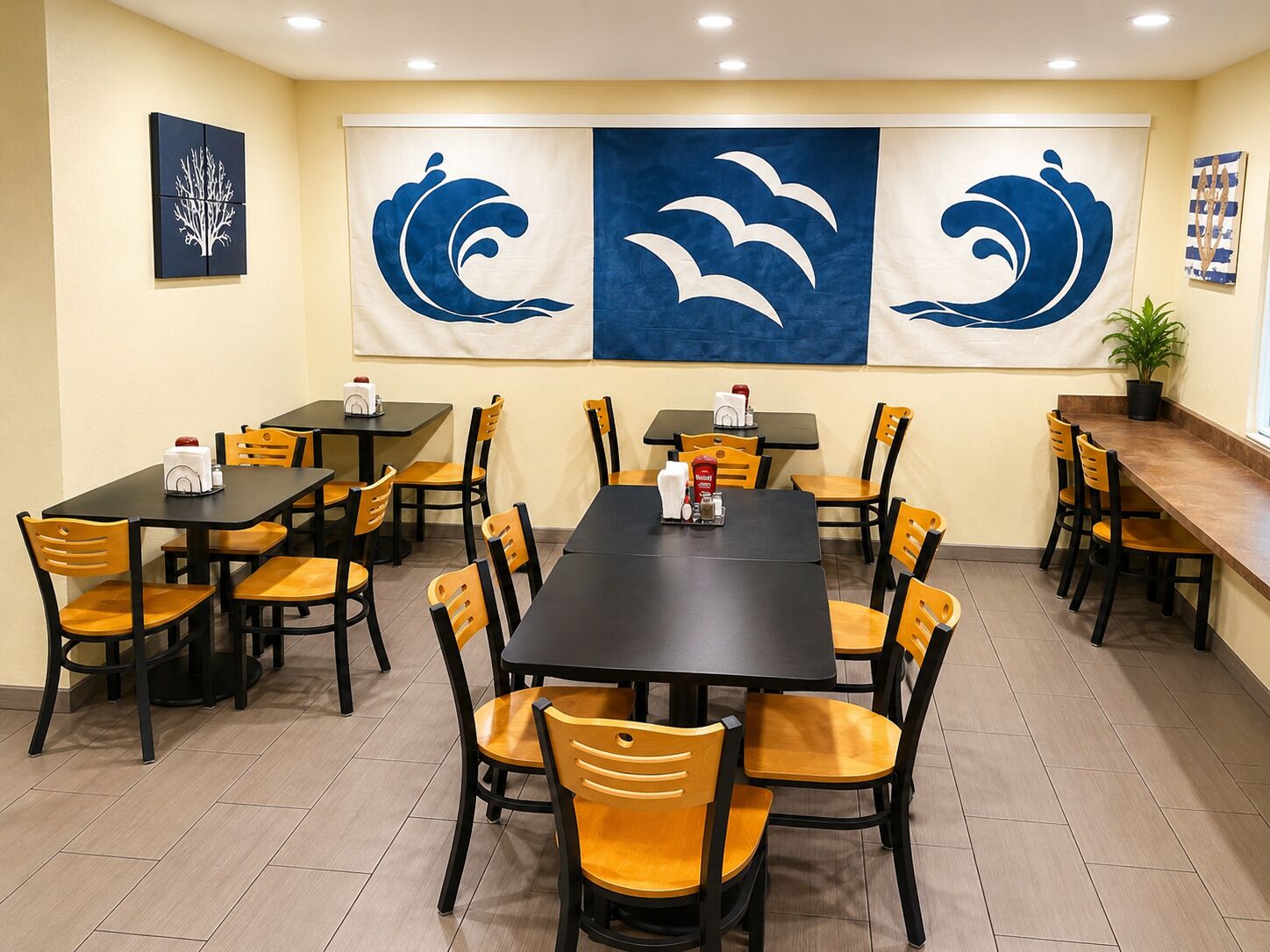 A restaurant with multiple tables and chairs, a large banner with wave designs, and a potted plant on the right.