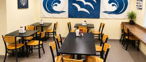 A restaurant with multiple tables and chairs, a large banner with wave designs, and a potted plant on the right.