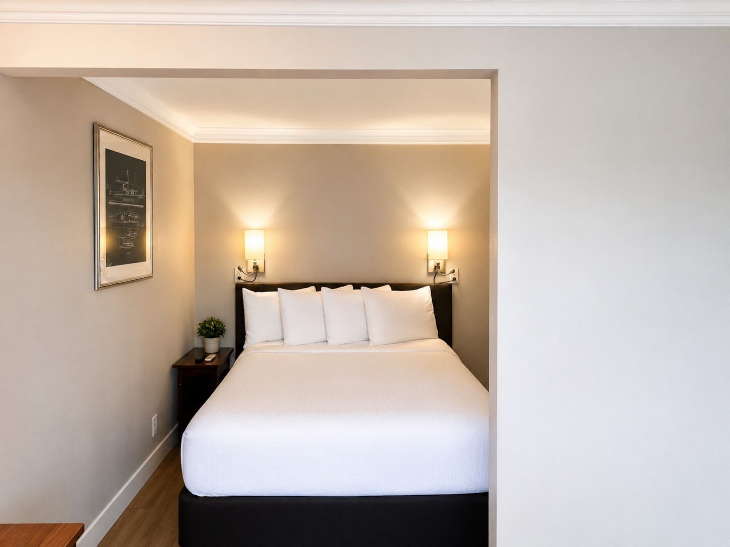 A hotel room with a bed, two bedside lamps, a nightstand, and a framed picture on the wall.