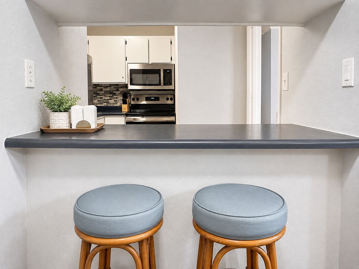 Una cocina con encimera oscura, electrodomésticos de acero inoxidable y dos taburetes de madera con cojines azules.