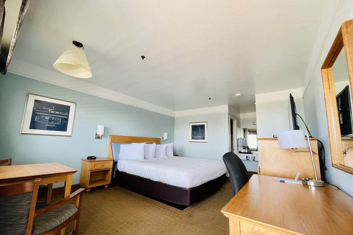 A hotel room with a bed, a desk, a chair, a lamp, and a framed picture on the wall.
