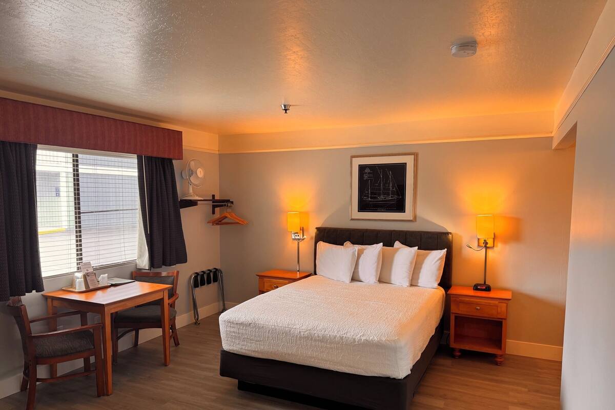 A hotel room with a bed, bedside tables, a desk, and a chair.