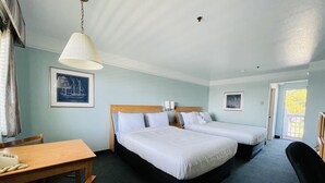 A hotel room with two beds, a wooden desk, a chair, a lamp, and a framed picture on the wall. - Seabird Lodge (Fort Bragg)