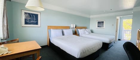 Habitación de hotel con dos camas, un escritorio de madera, una silla, una lámpara y un cuadro en la pared.