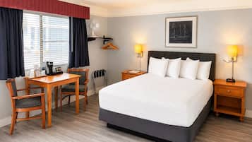 Habitación de hotel con cama, mesitas de noche, un escritorio con sillas, una ventana con cortinas y un cuadro colgado en la pared.