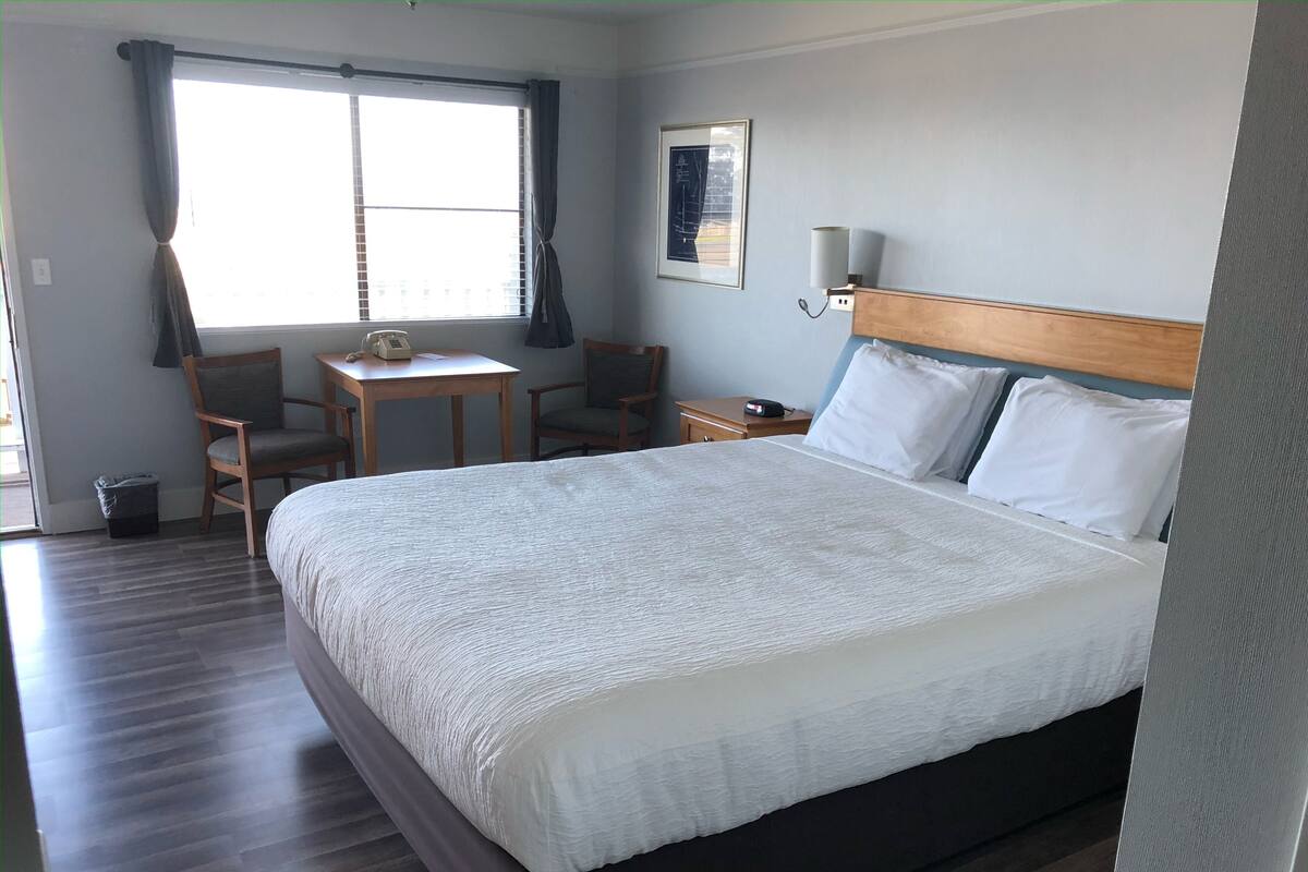 A neatly arranged hotel room with a large bed, a desk, two chairs, a small table, and a window with curtains.