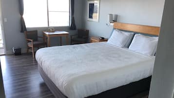 Habitación de hotel ordenada con una cama grande, un escritorio, dos sillas, una mesita y una ventana con cortinas.