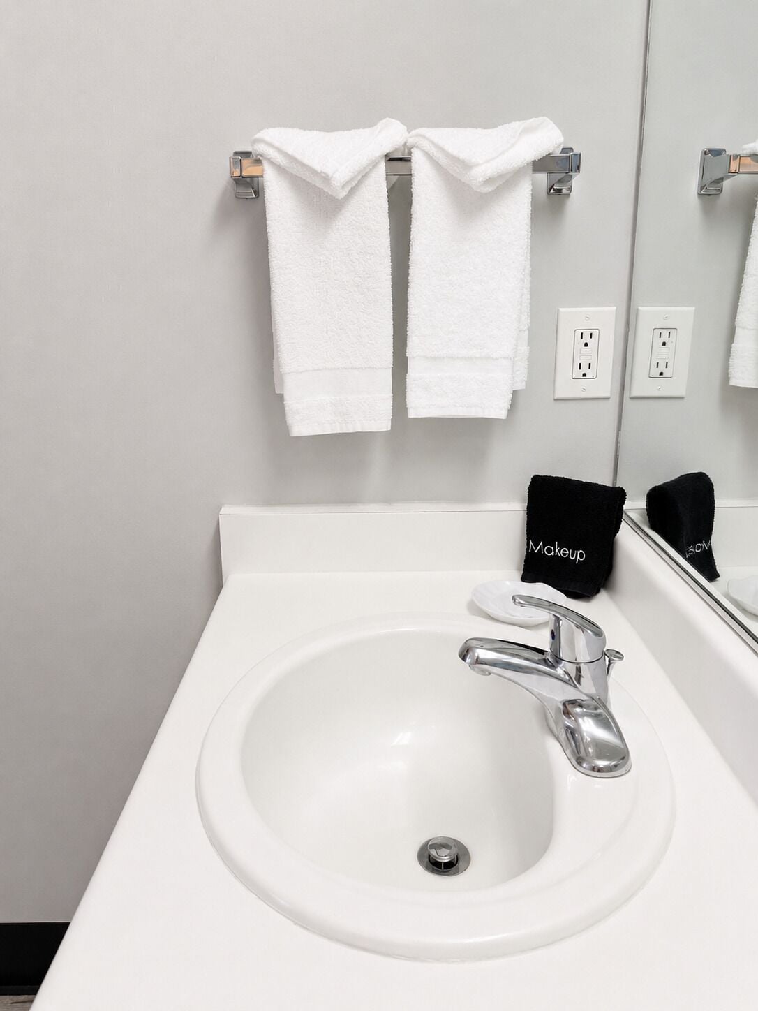 A bathroom with a white sink, a mirror, and two white towels hanging on a towel rack.
