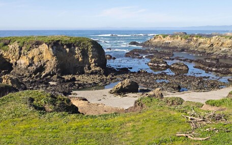 A coastal landscape with rocky cliffs, a sandy beach, and the ocean.
