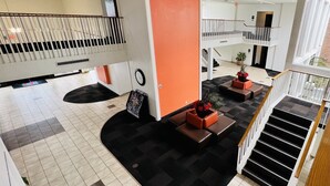 A spacious lobby with a checkered floor, a staircase, and a modern orange accent wall. - Motel 6 Irvine - Orange County Airport (Santa Ana)