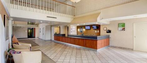 Un hall de hotel con mostrador de recepción, zona de estar y una escalera que conduce a un nivel superior.