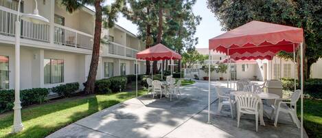 A courtyard with outdoor seating, a white building, and a red canopy.