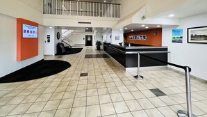 A spacious lobby with a reception desk, a staircase to an upper level, and a sign welcoming smart travelers. - Motel 6 Irvine - Orange County Airport (Santa Ana)