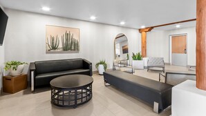 A modern living room with a black sofa, a round coffee table, and a large cactus painting on the wall.