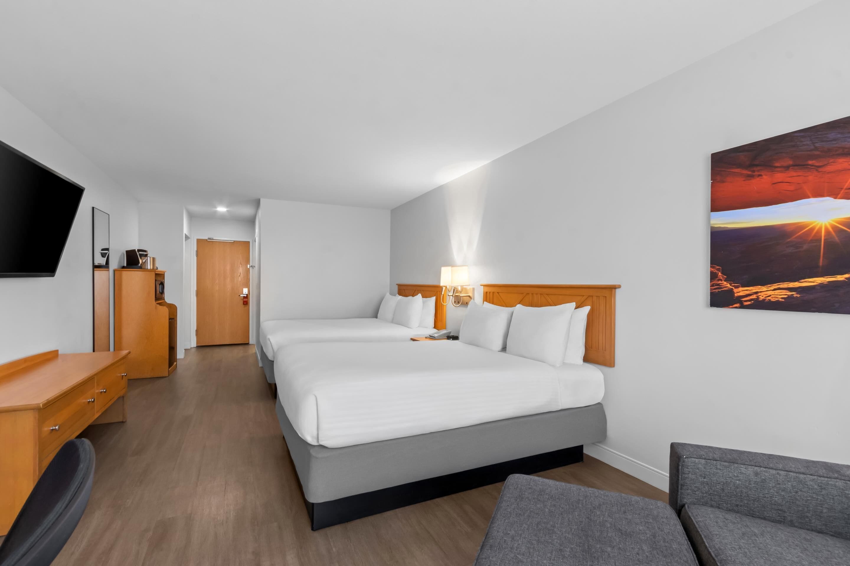 Habitación de hotel con dos camas, televisión, escritorio y un cuadro de un atardecer.
