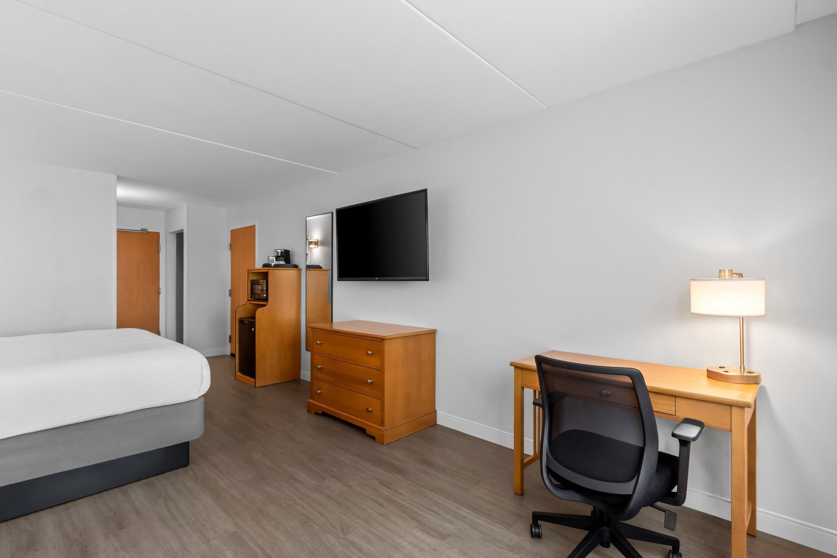 Een hotelkamer met een bed, bureau, stoel, televisie en lamp.