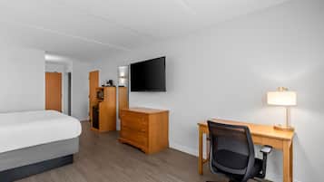 Een hotelkamer met een bed, bureau, stoel, televisie en lamp.