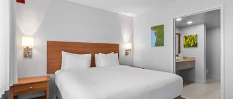 A hotel room with a large bed, bedside lamps, a wooden nightstand, a bathroom with a sink and mirror, and a door leading to another room.