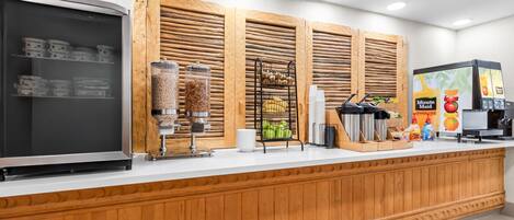 Un espace de libre-service proposant des boissons, avec un présentoir réfrigéré, une machine à café et divers produits alimentaires.