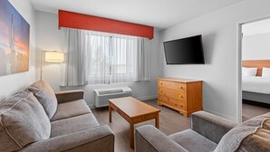 A hotel room with a sofa, a wooden table, a dresser, a TV, and a window with curtains.