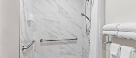A shower with a glass door, a wooden bench, and a towel rack with folded towels.